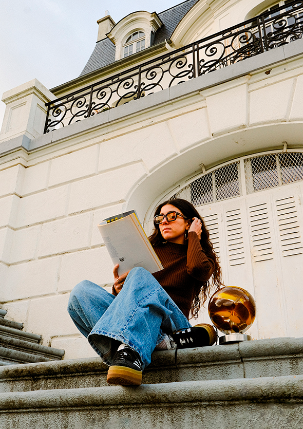 Femme en train de lire assise sur escaliers avec lampe posée à côté