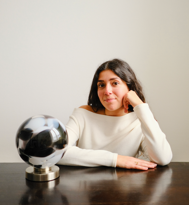 Femme brune accoudée à une table avec une lampe posée sur la table
